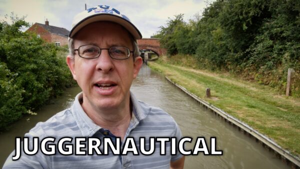 The video's host, David, is staring at the camera lens while he steers his narrowboat away from a bridge. The video is titled Juggernautical.